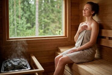 Frau entspannt in Sauna mit Blick nach draußen auf Natur.