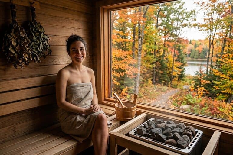 Entspannende Frau in Sauna mit Blick auf herbstliche Natur.
